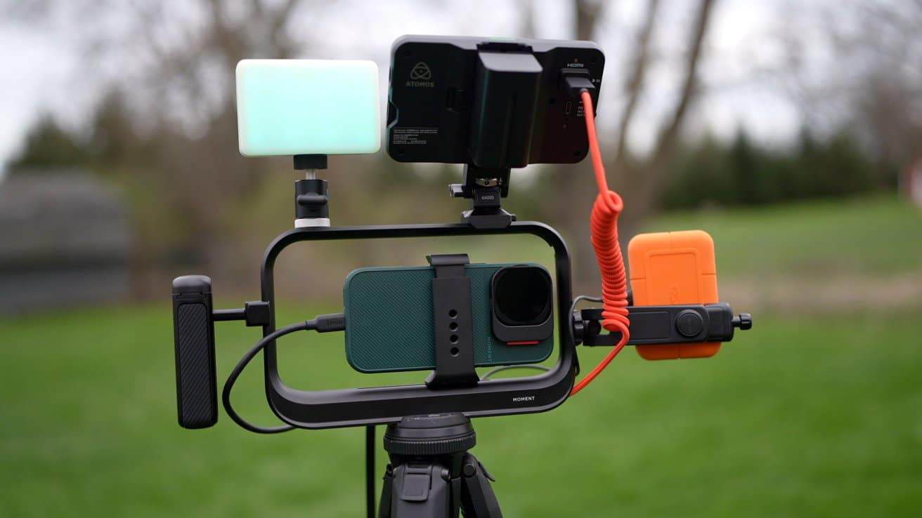 A smartphone rig with a camera, monitor, lights, and external hard drive on a tripod in an outdoor setting.