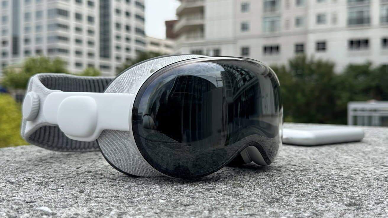 A sleek, futuristic virtual reality headset with a reflective visor lies on a concrete surface, against a backdrop of blurred buildings and greenery.
