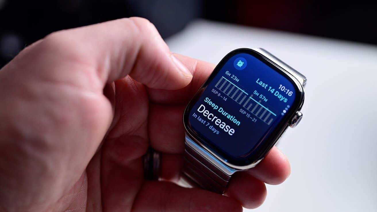 A hand holding a smartwatch displaying sleep data, including bar graph and text indicating a decrease in sleep duration over the last seven days.