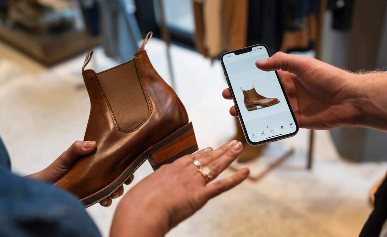 Hands holding a brown boot and a smartphone displaying a matching boot design.