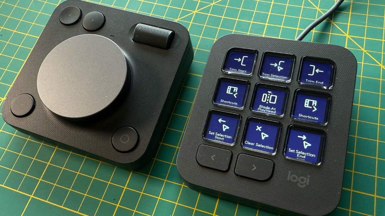 Two black devices on a green grid mat, one with a large dial and buttons, the other with illuminated buttons labeled for editing functions.