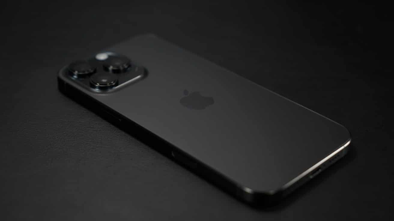 A black smartphone with three camera lenses on a dark surface, displaying the Apple logo.