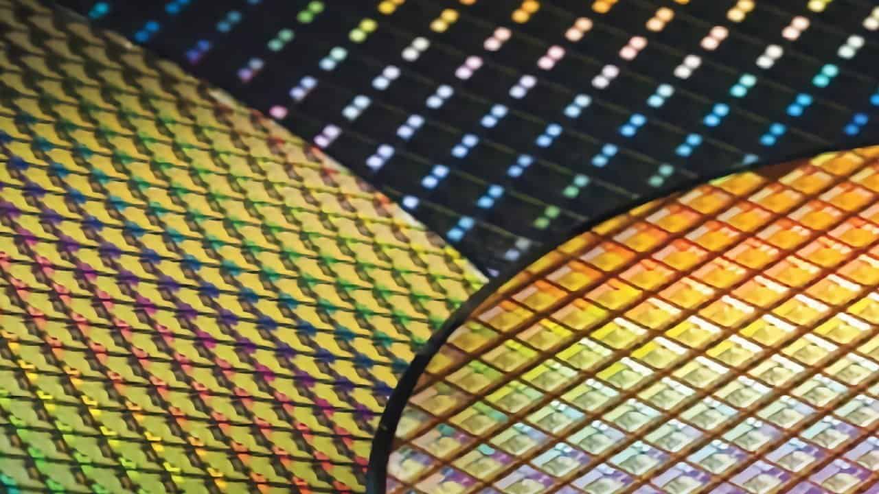 Close-up of colorful semiconductor wafers showcasing intricate, reflective patterns in vibrant rainbow hues on a dark background.