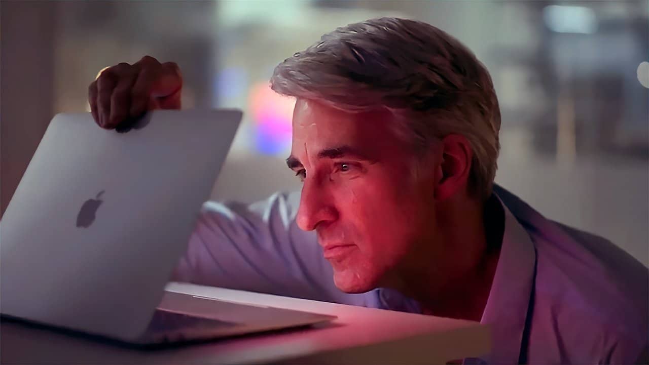 A person with silver hair attentively looks at an open laptop, which reflects a soft, colorful light on their face, in a dimly lit room.