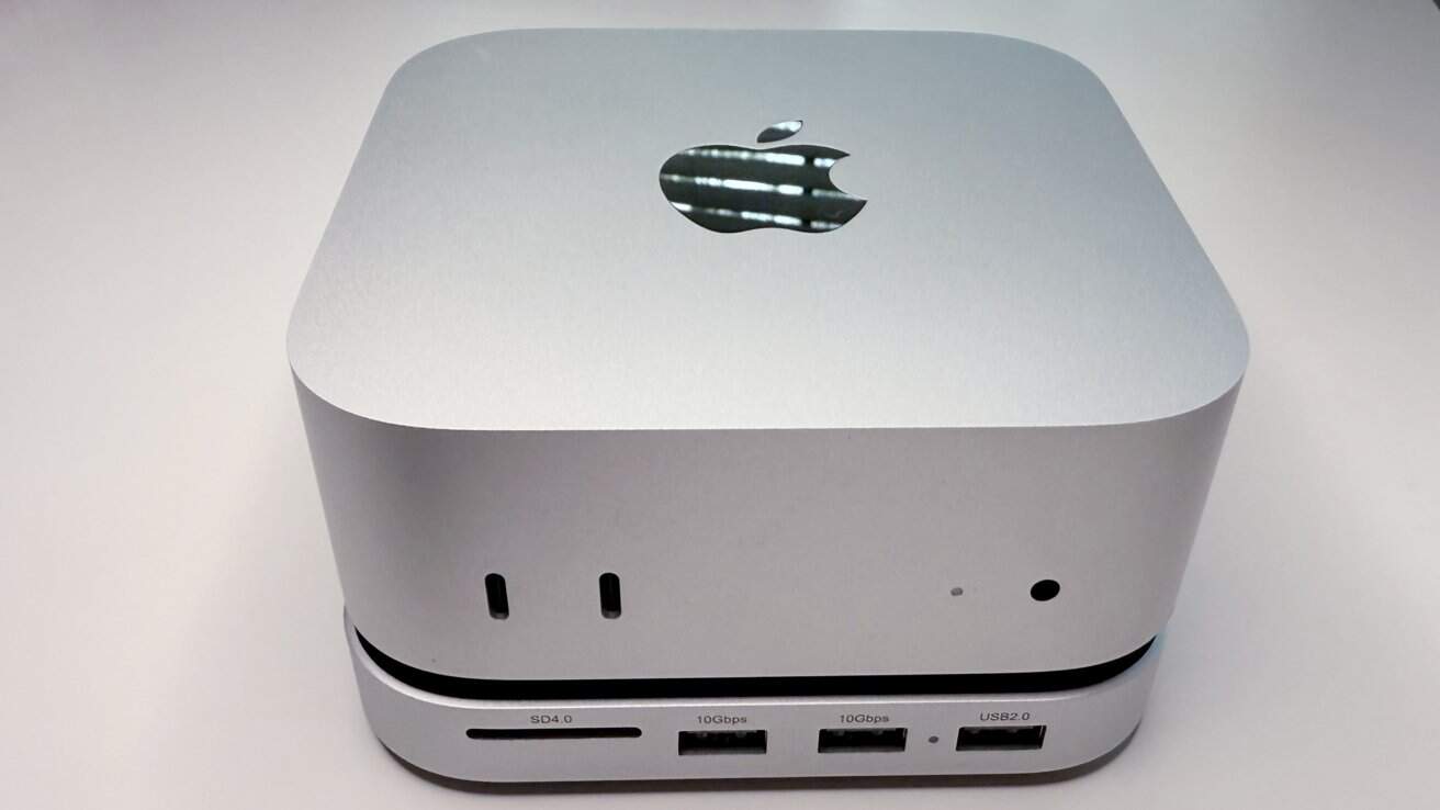 A sleek silver computer device with rounded edges, featuring an Apple logo on top, multiple ports, and a minimalist design.