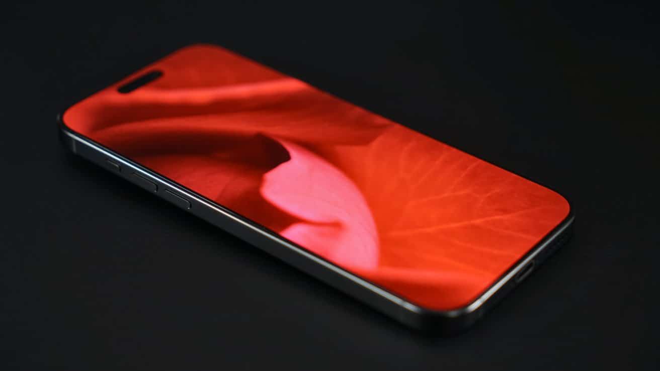 Smartphone with a vibrant red-orange floral pattern on the screen, placed on a dark surface.