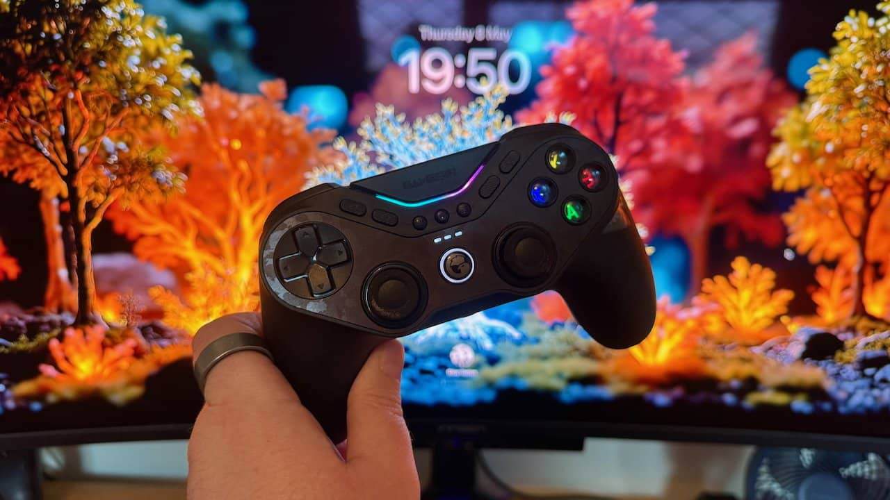 Hand holding a black Tarantula Pro controller in front of a vibrant colorful landscape on a screen, featuring orange and blue foliage.