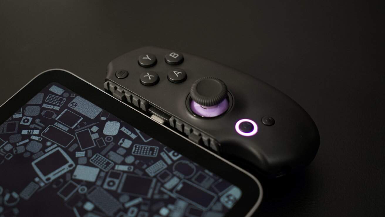 Tablet with a geometric patterned screen and attached black gaming controller featuring buttons and a joystick on a dark surface.