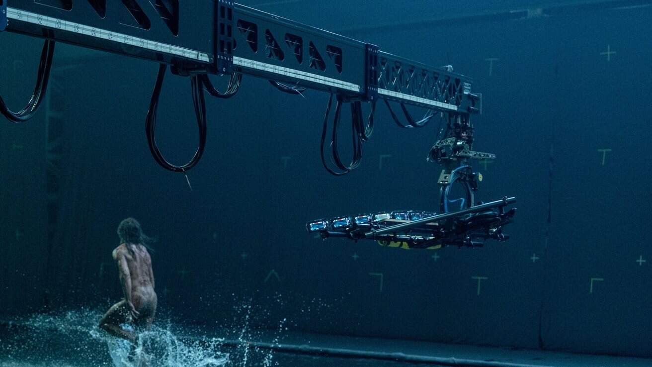 Large robotic camera crane over water as a person runs, causing splashes.