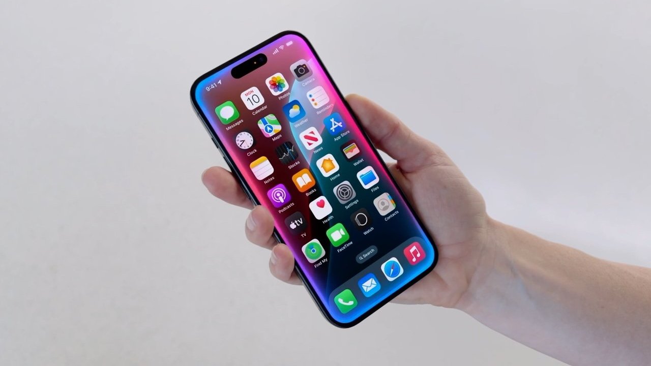 Hand holding smartphone with colorful app icons on the screen, against a plain background.