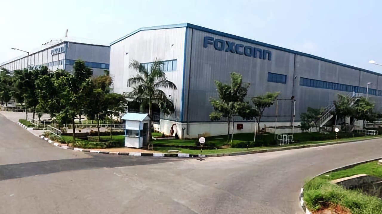 Large industrial building labeled Foxconn, surrounded by trees and greenery, with an adjacent road leading to multiple entrances.