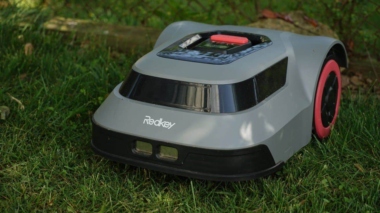A gray robotic lawn mower with red wheels and a black trim, labeled 'Redkey,' on green grass.