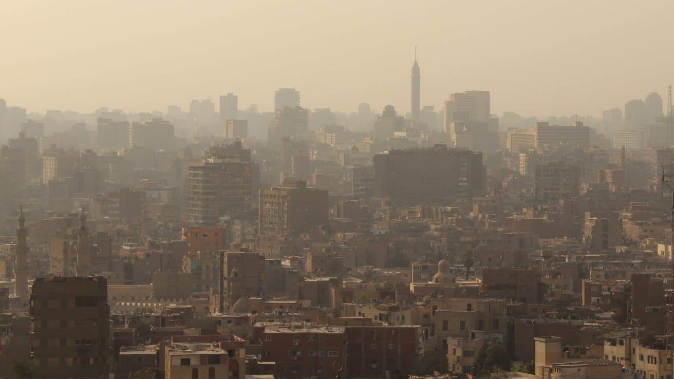 Distant view of a city skyline with numerous tall buildings and a prominent tower against a hazy sky.