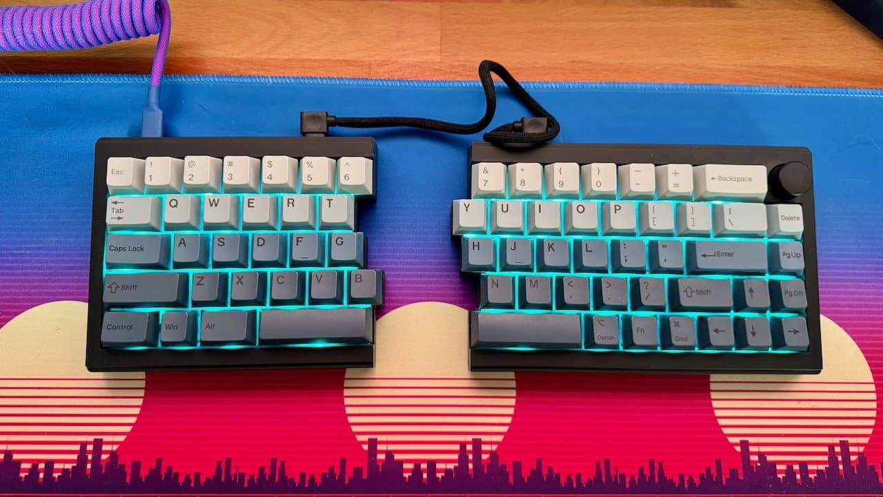 Split keyboard with blue backlight on colorful pad displaying city skyline and sunset design.