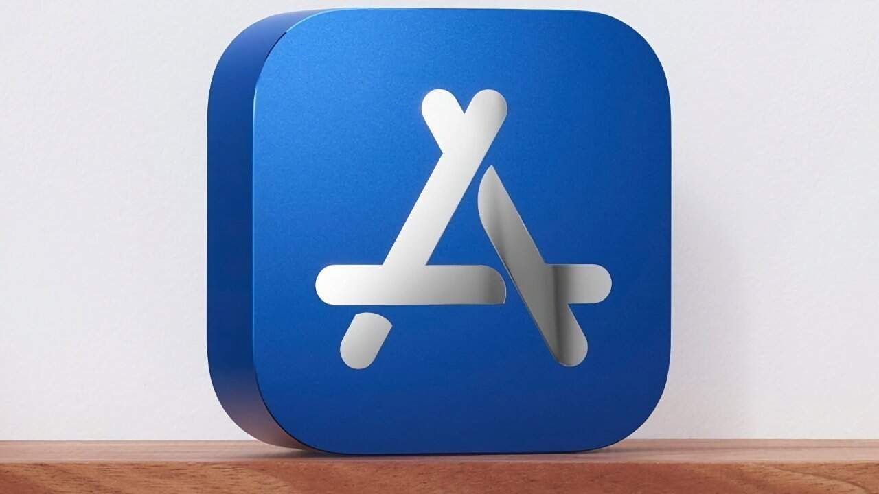 Blue cube with rounded edges featuring a white 3D overlapping sticks design resembling the App Store logo, placed on a wooden surface.