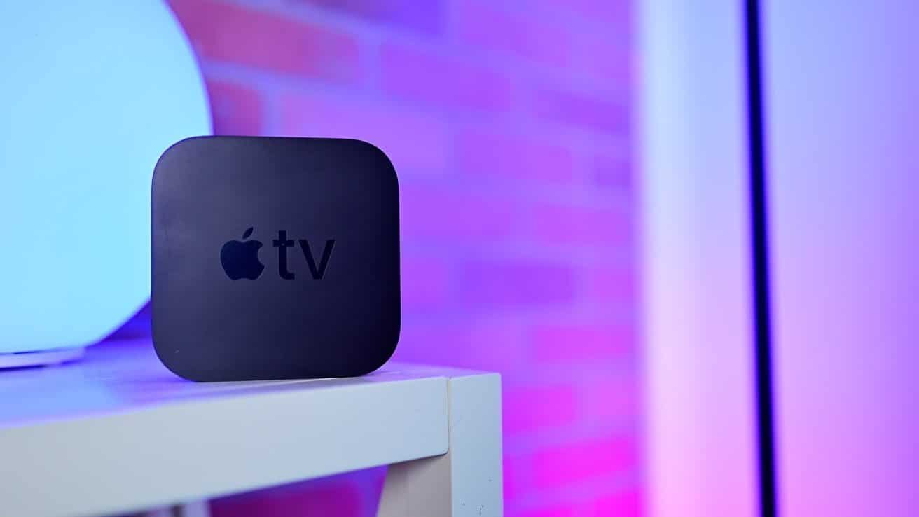 Black Apple TV device on a white table against a gradient background of blue and pink hues with a blurred brick pattern.