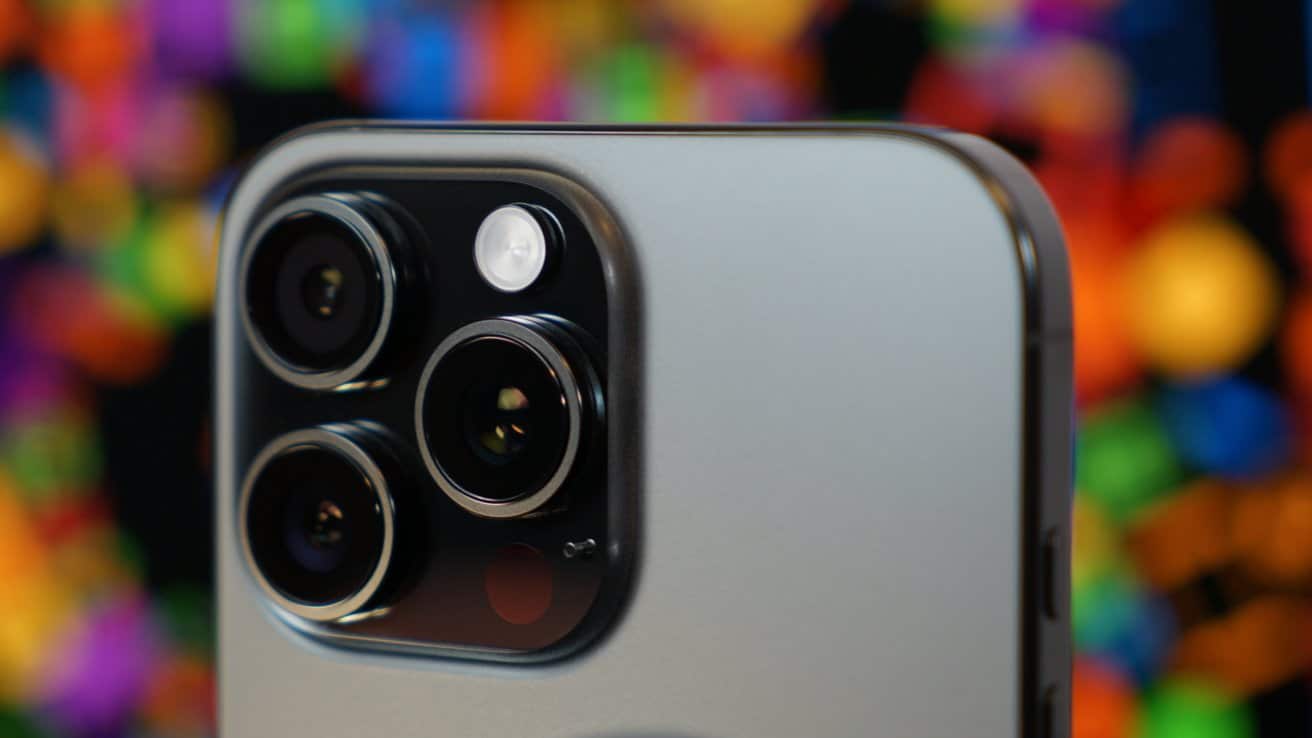 Close-up of a smartphone's triple-lens camera with colorful blurred lights in the background.