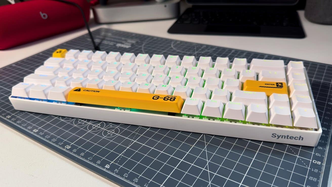 White mechanical keyboard with green backlighting and yellow novelty keycaps labeled 'Caution' and 'Enter,' placed on a cutting mat.