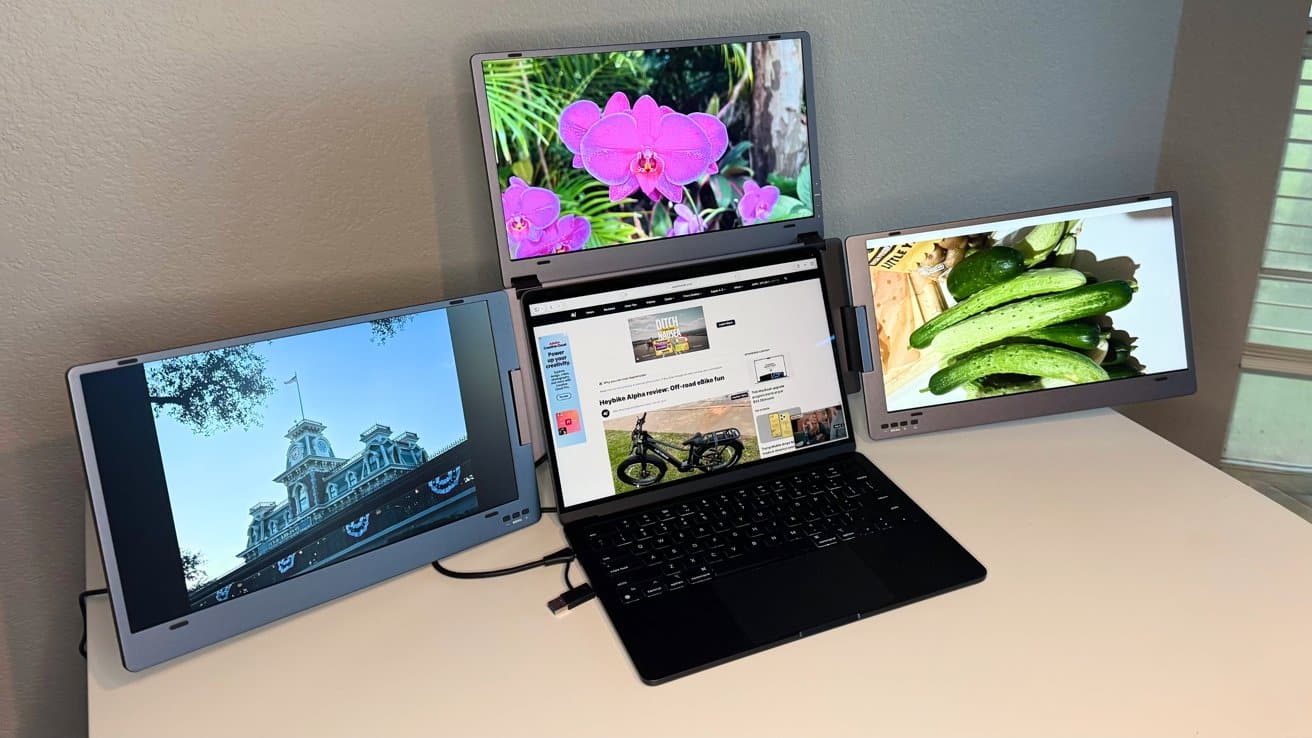 A laptop with a triple-screen setup displays a website, pink flowers, a historic building, and cucumbers on each connected monitor, on a white desk.