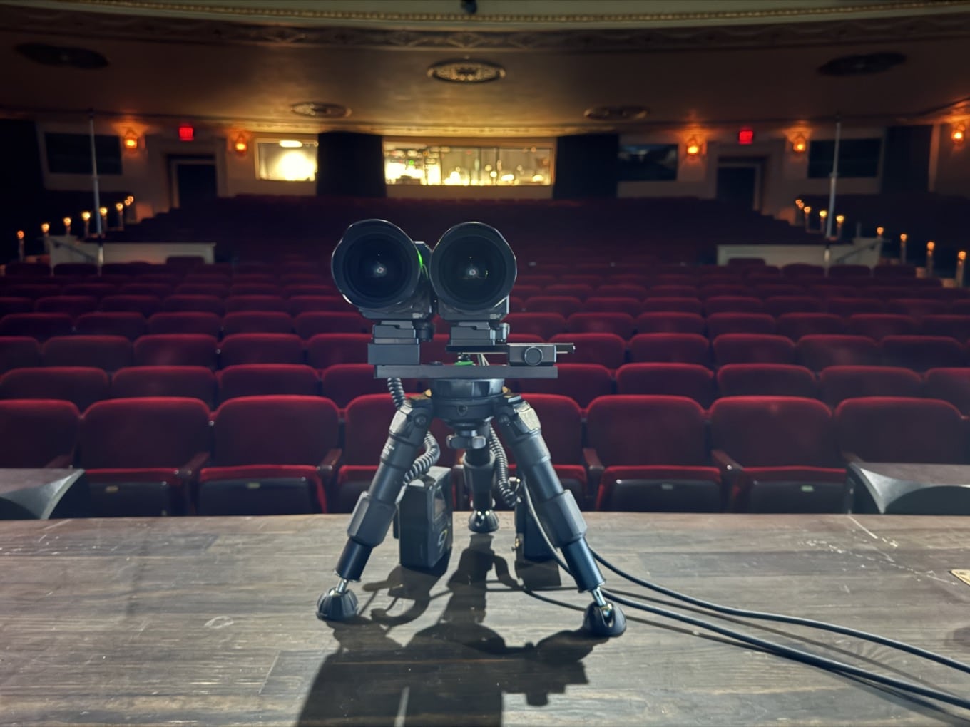 A camera on a tripod in an empty theater with red seats.