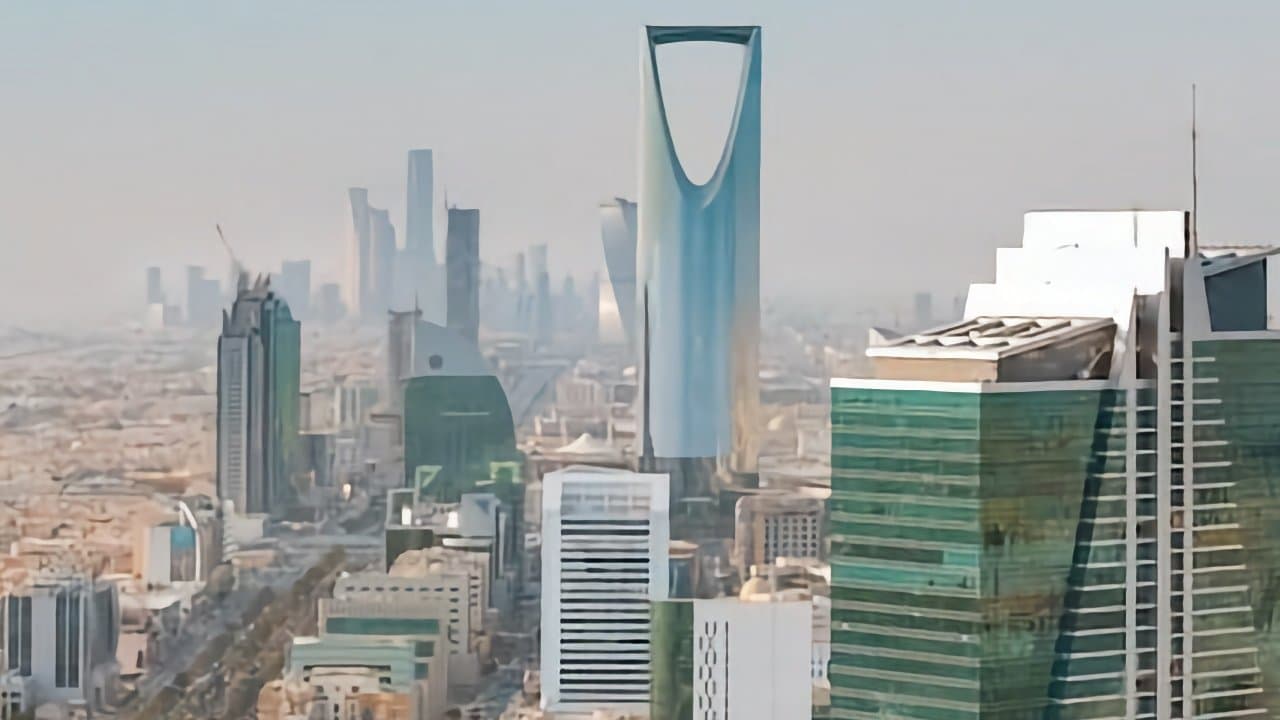 City skyline featuring modern skyscrapers, including a tall, uniquely-shaped tower with a curved opening at the top, under a clear sky.