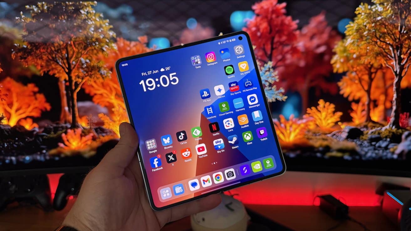 A hand holds a foldable smartphone displaying apps, with a vibrant, colorful background of autumnal trees and bokeh lighting effects.