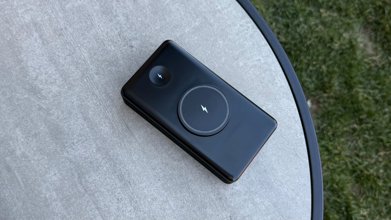 A black wireless charger on a round table with a gray surface, surrounded by grass.