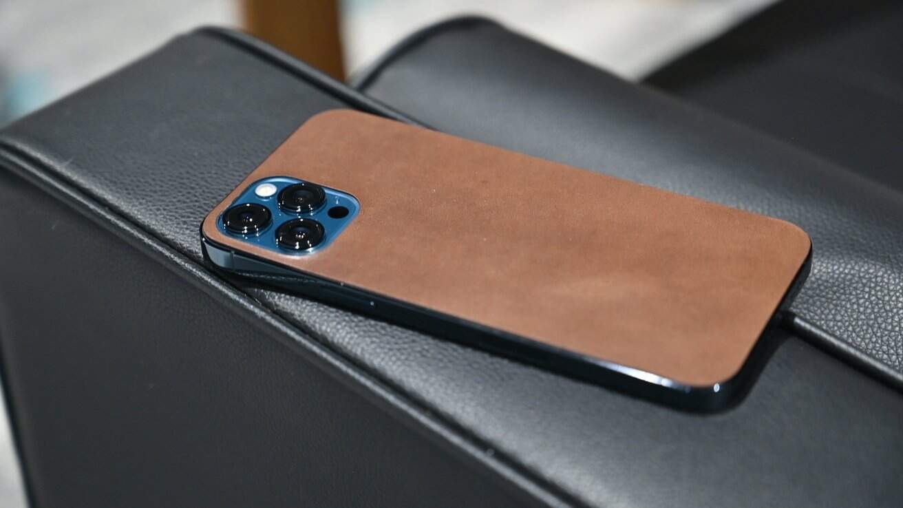 Smartphone with a brown leather case and three camera lenses, resting on a black leather surface.