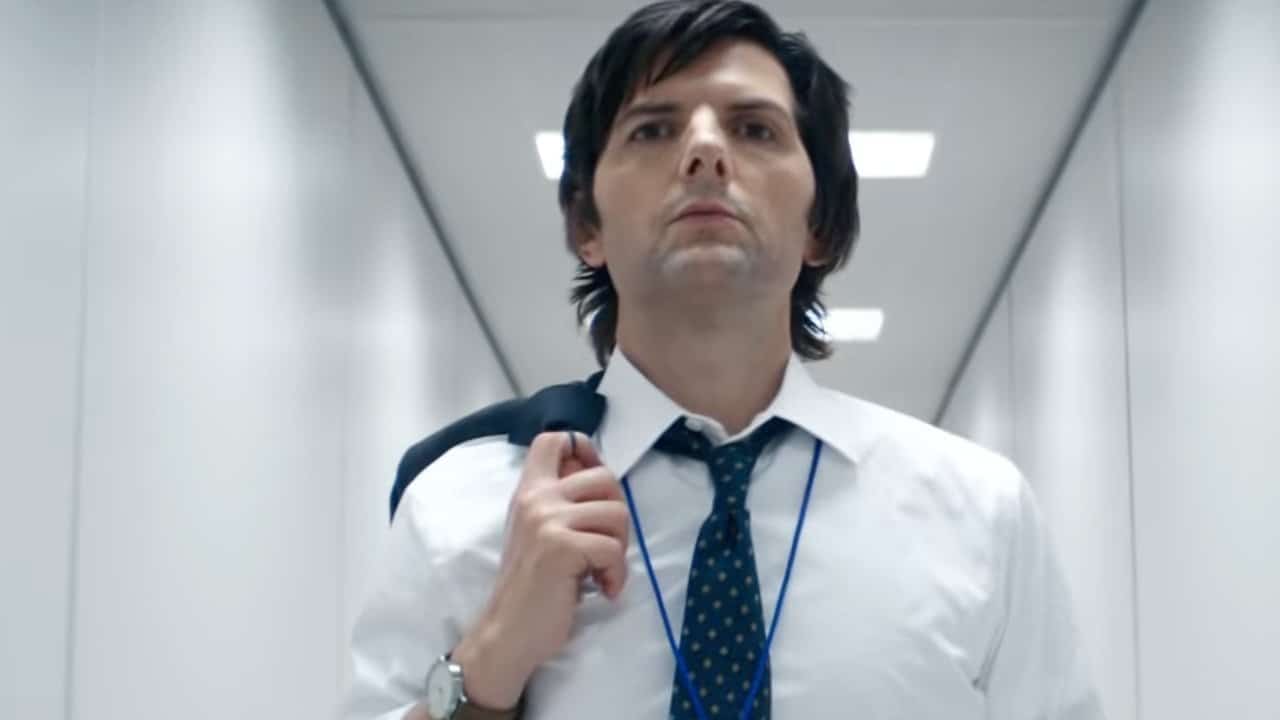 A man in a white shirt and tie walks confidently down a well-lit, white hallway, carrying a jacket over his shoulder.