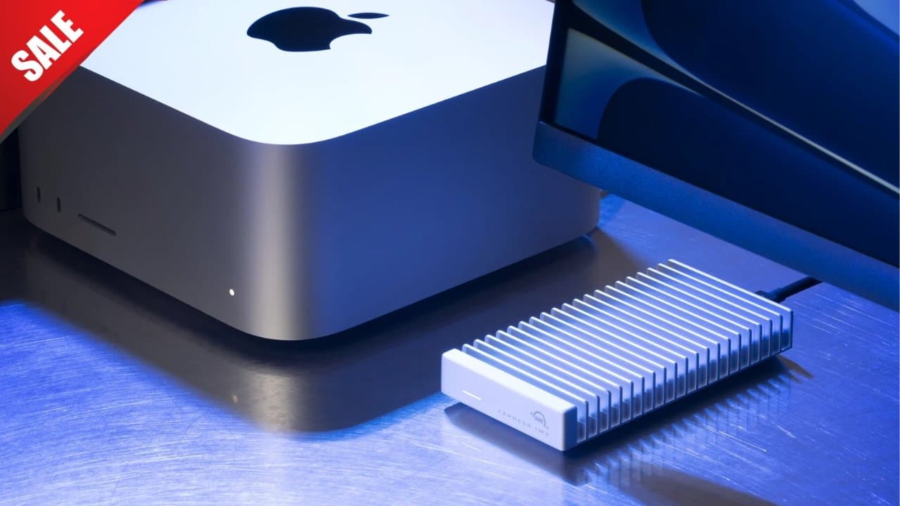 Mac Studio setup with an OWC Express 1M2 external SSD and a monitor on a sleek blue-lit surface. Red sale banner in the corner.