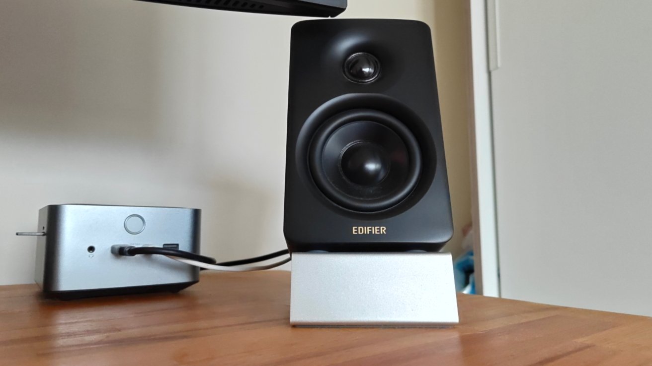 A black speaker labeled 'Edifier' on a wooden surface next to a small metal electronic device with cables connected.