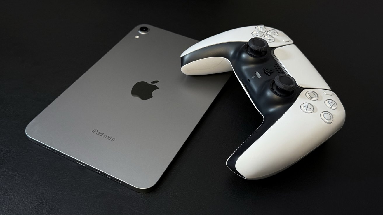 A gray tablet with an Apple logo lies next to a white and black game controller on a dark surface.