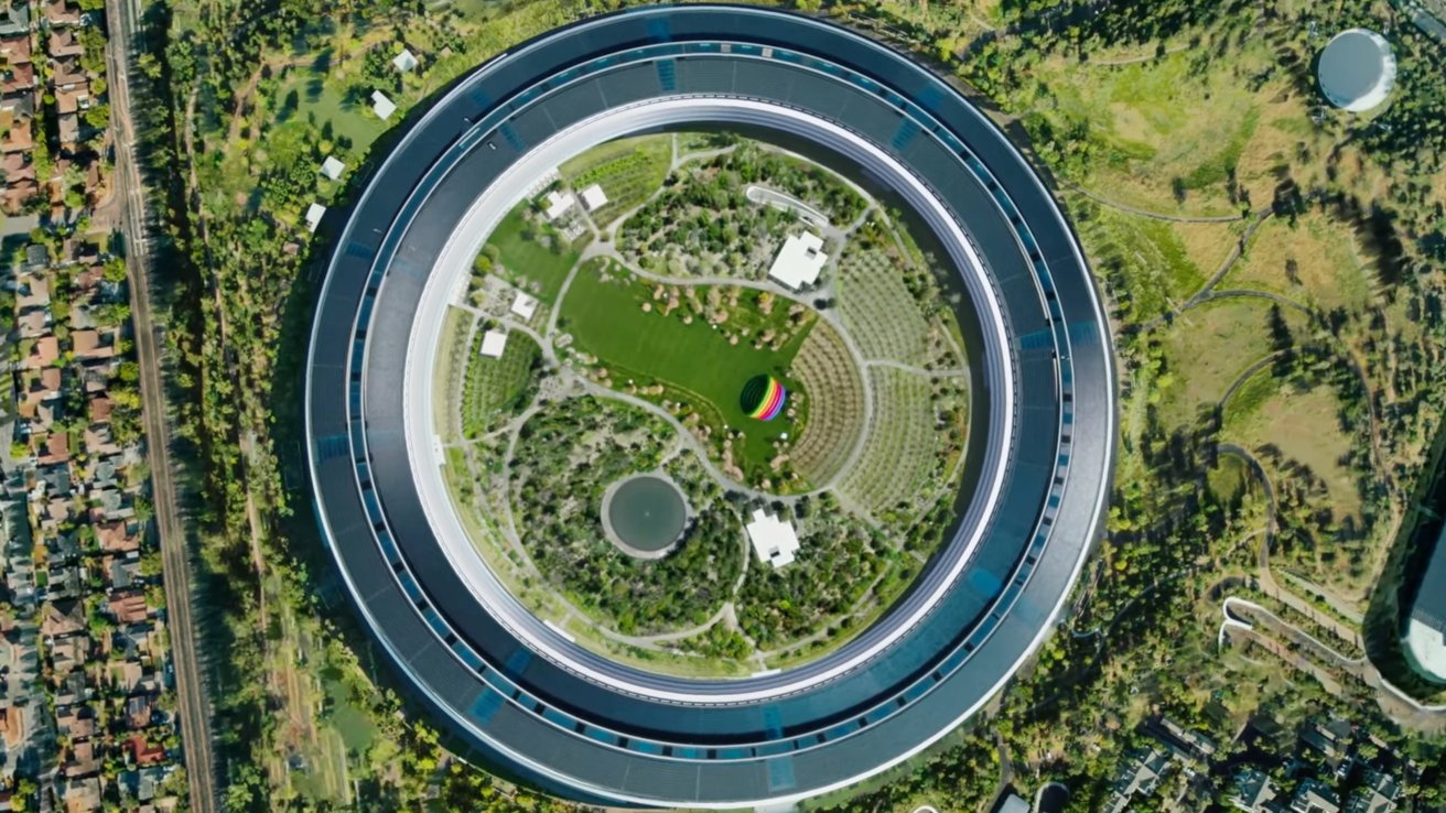 Aerial view of a circular building surrounded by trees, featuring a lush green center with pathways and small white structures.