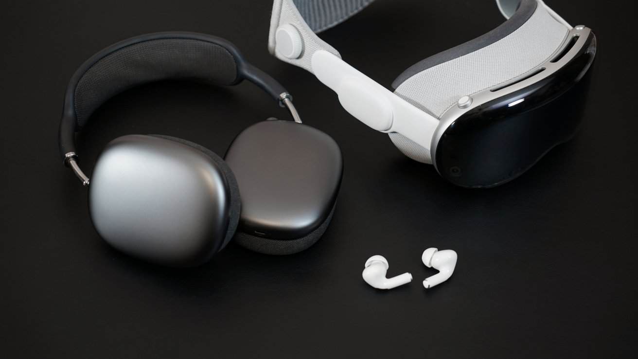 On a black table, AirPods Max next to Apple Vision Pro and AirPods Pro lying outside of their case