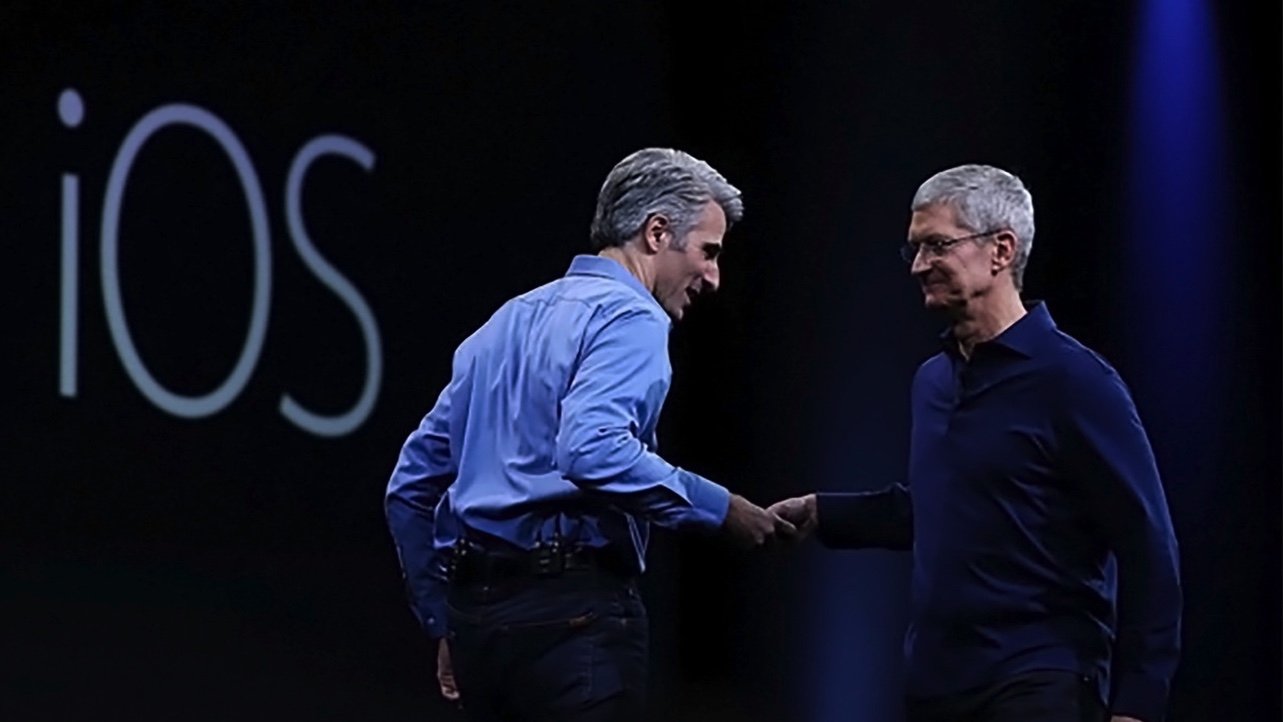 Two people in formal attire shaking hands on stage, with 'iOS' displayed in the background.