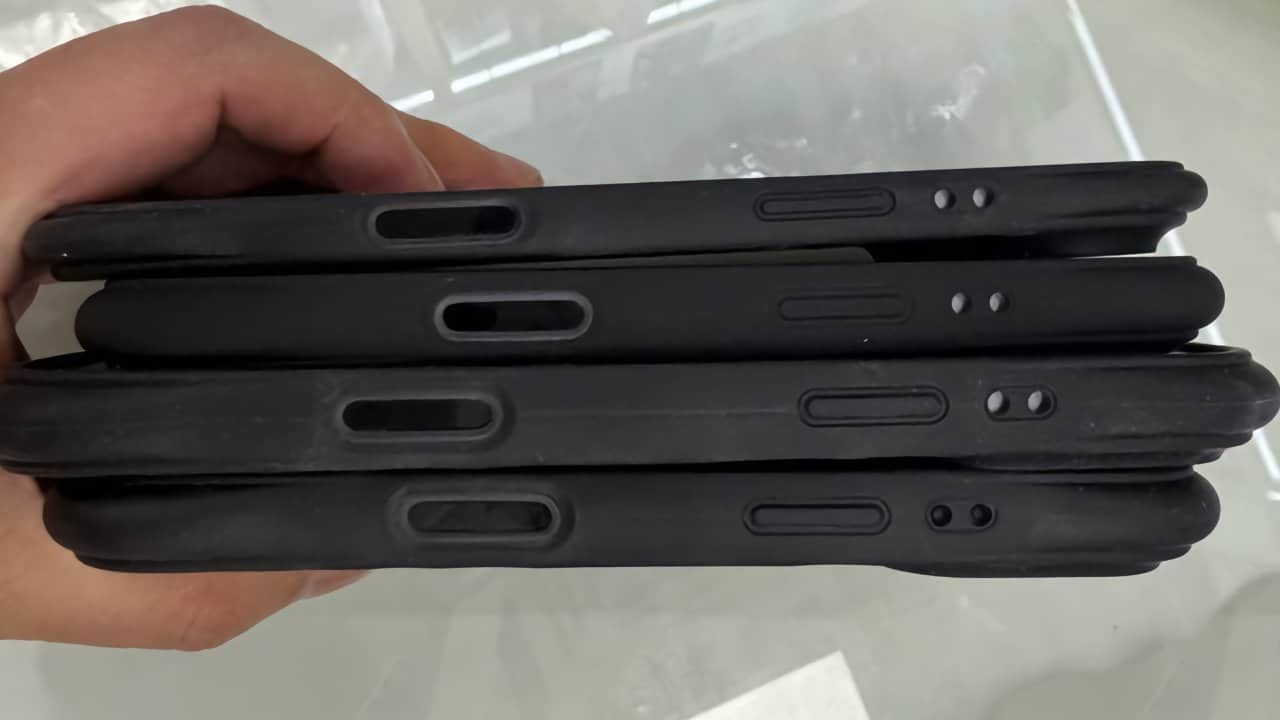 Hand holding four stacked black tablets or smartphones with protective cases and visible side buttons.
