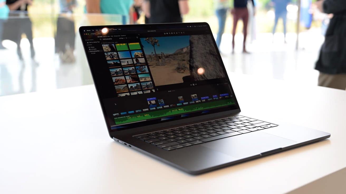 A laptop on a white table, displaying video editing software with thumbnails and a timeline. Individuals stand blurred in the background.