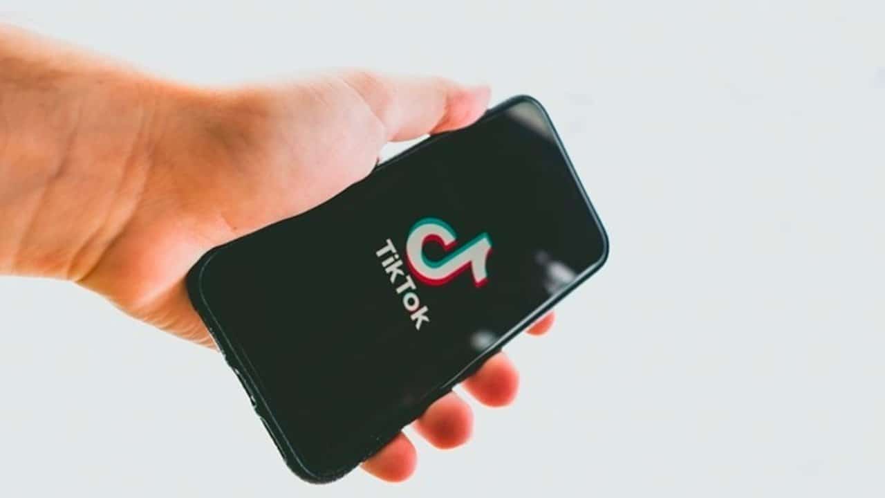 A hand holds a smartphone displaying the TikTok logo on its screen against a white background.