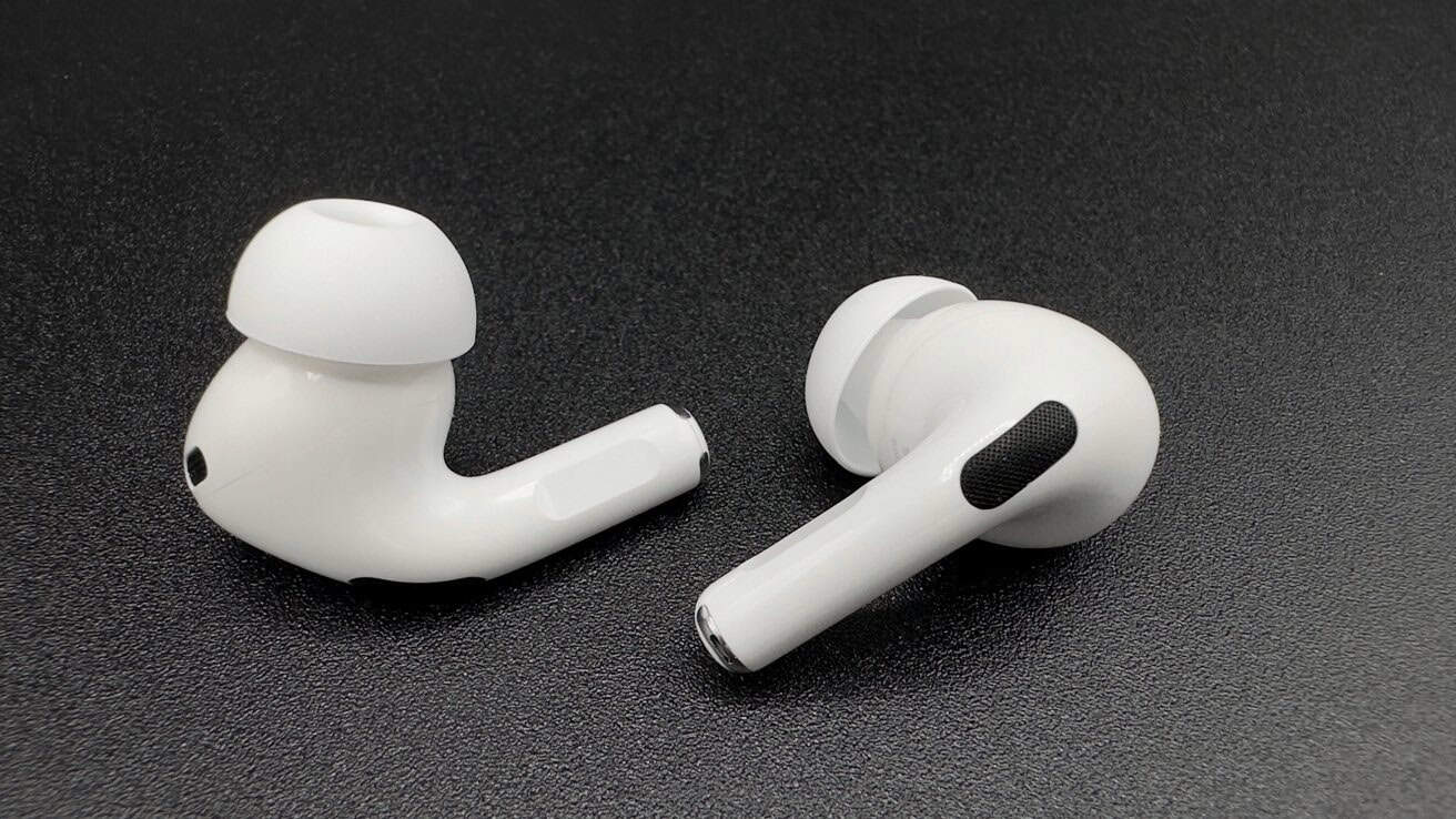 Two white wireless earbuds with black accents resting on a dark textured surface.
