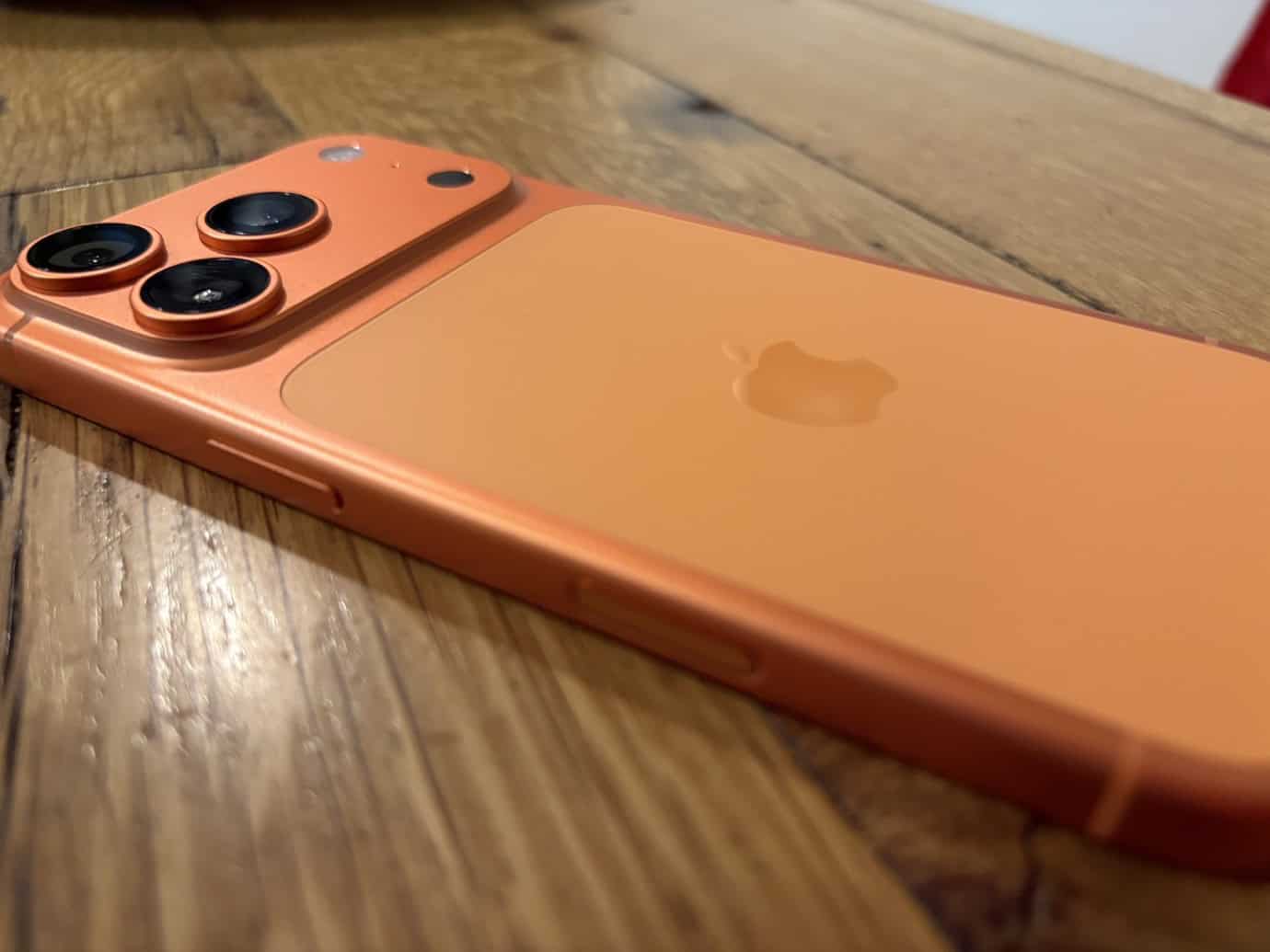 Orange iPhone with triple camera on a wooden surface.