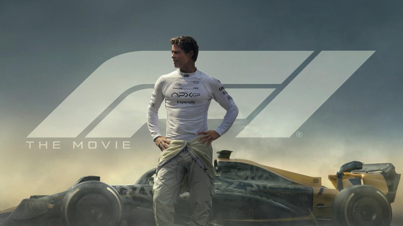 A man in a racing suit stands confidently in front of a Formula 1 car. The background features a large stylized 'F1' logo. Text reads 'THE MOVIE.'