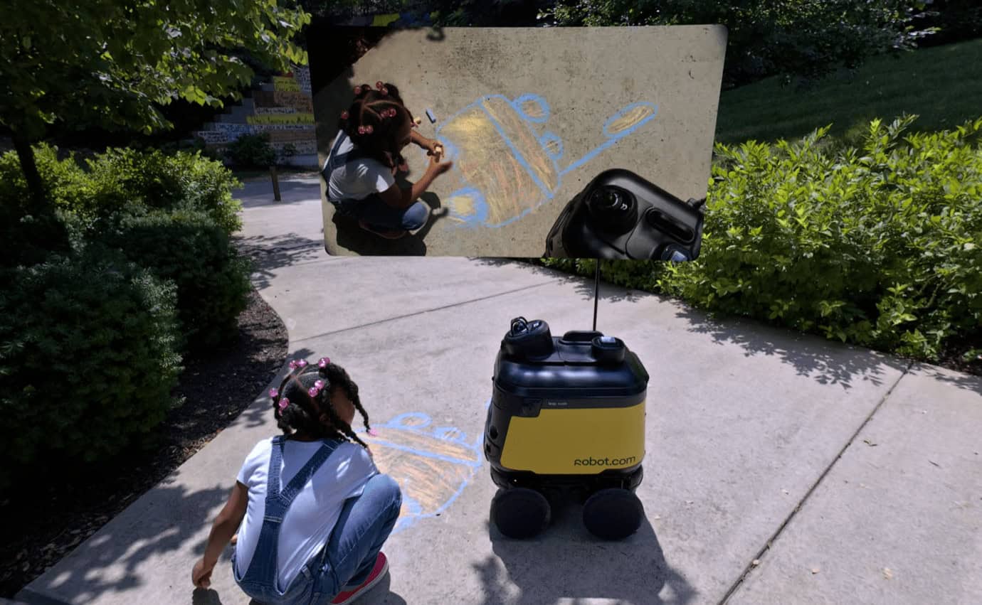 Two children and a robot on a sidewalk near a wall with chalk art. One child is drawing on the wall, while the other kneels nearby. The robot has a screen and wheels.