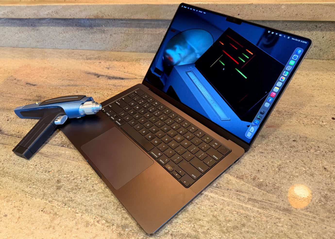 A laptop with a sci-fi scene on the screen next to a blue and black handheld device on a wooden surface. Star Trek references!