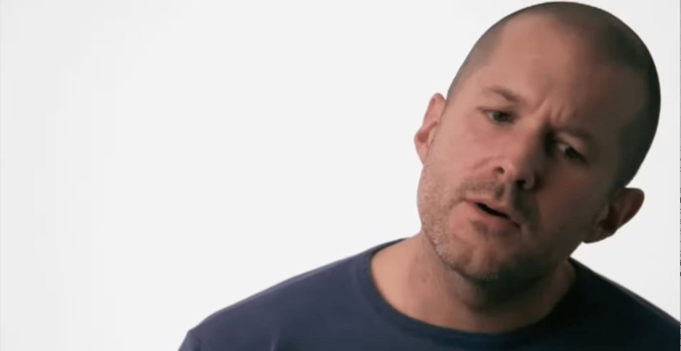 Bald man in a blue shirt with a confused expression, looking slightly to the side against a white background.