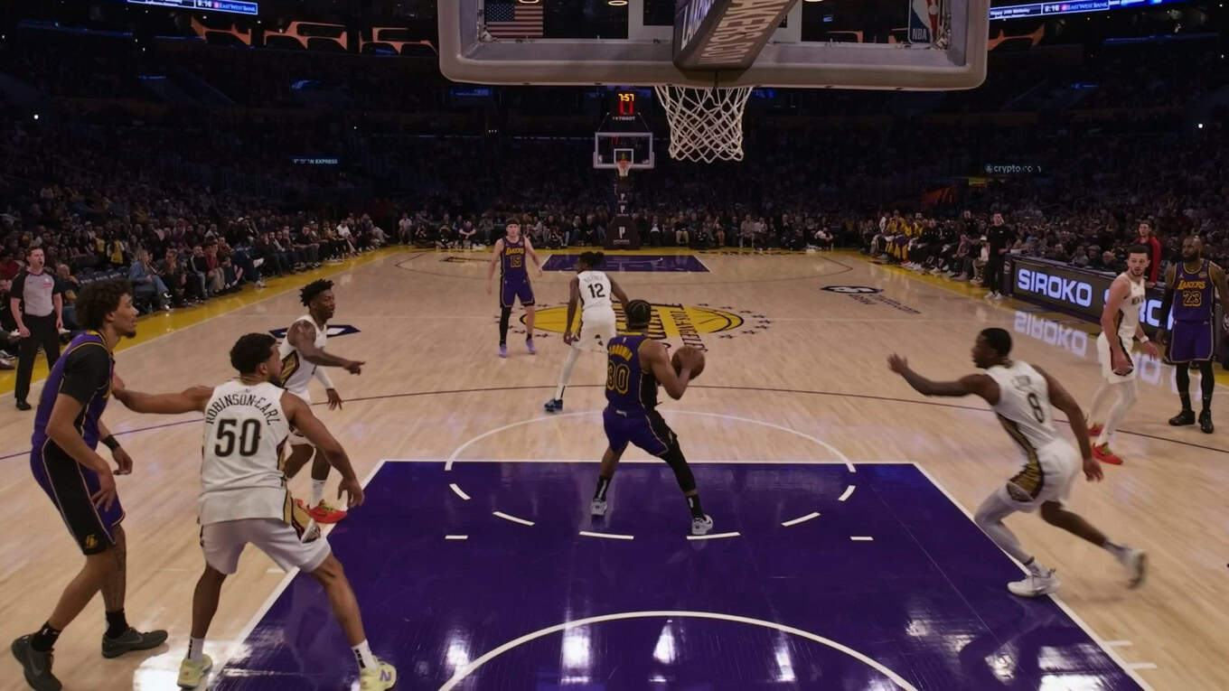 Basketball game in progress at a large arena. Players in purple and white uniforms compete near the basket.