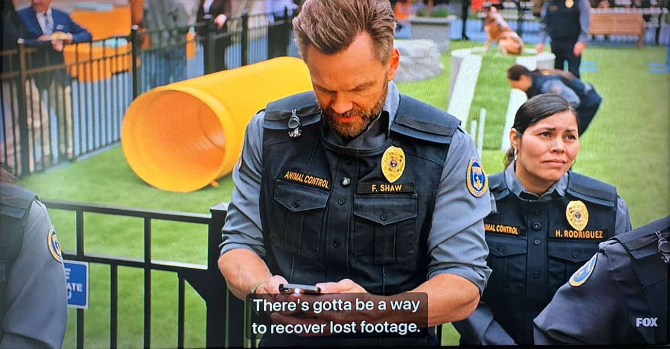 Two animal control officers in uniforms stand outdoors near a yellow slide. One officer looks at a device, saying, 'There's gotta be a way to recover lost footage.' A 'FOX' logo is visible.
