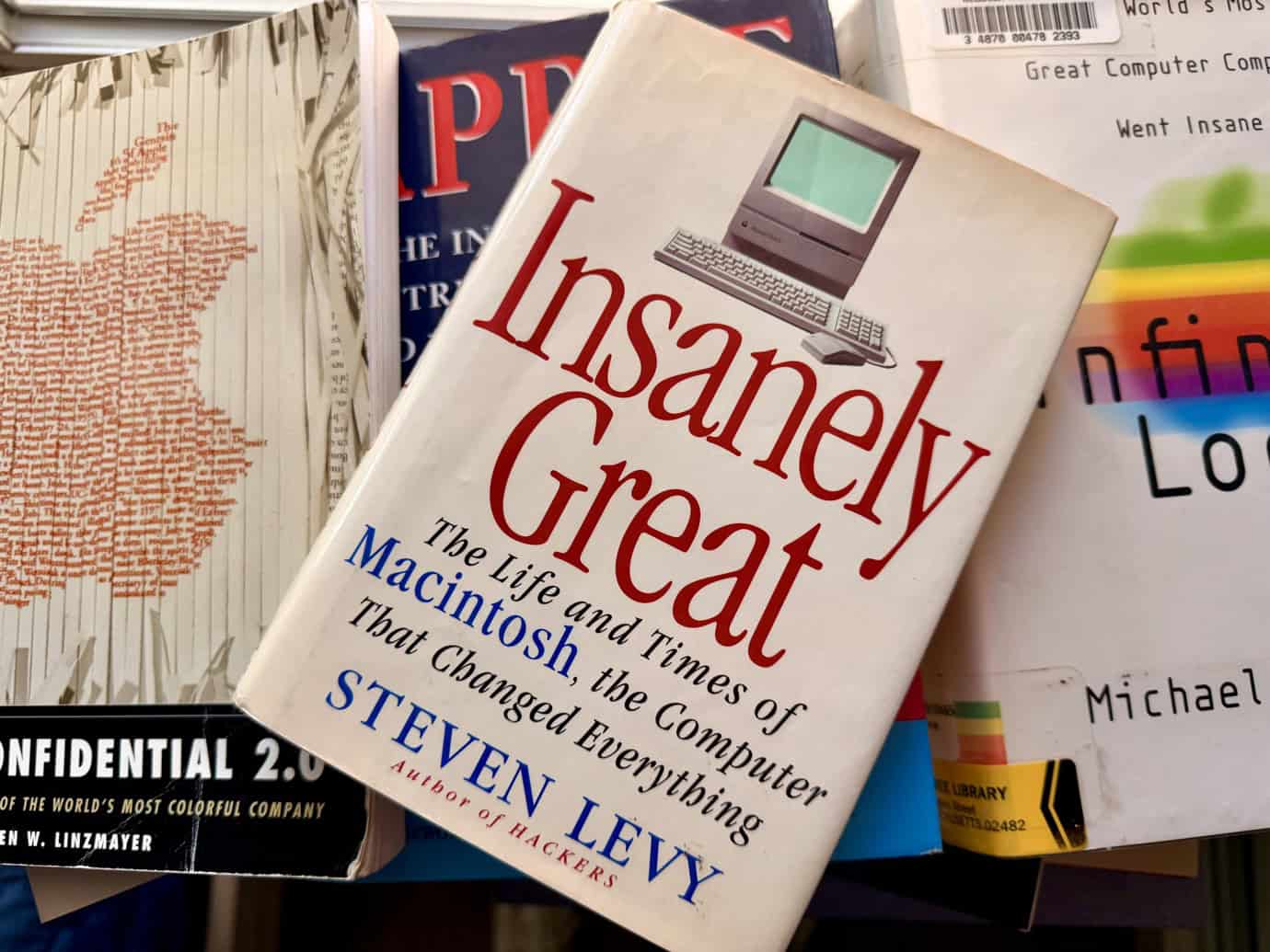 A book titled 'Insanely Great: The Life and Times of Macintosh, the Computer That Changed Everything' by Steven Levy, featuring a vintage computer illustration, is prominently displayed among other books.