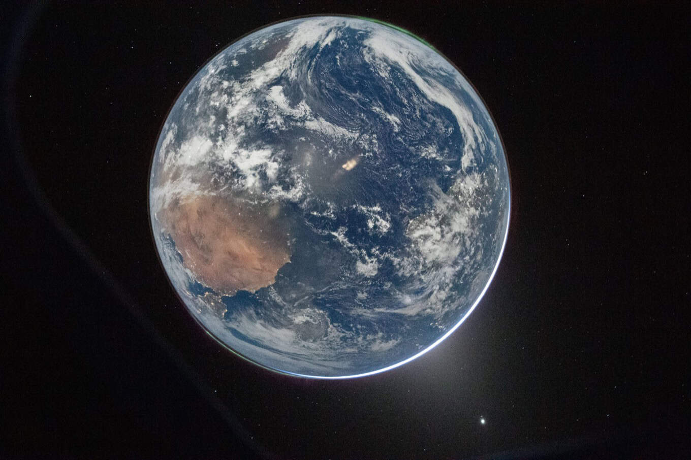Earth from space, showing Africa's western coast and swirling white clouds over blue oceans. The planet is partially illuminated by sunlight against a black background.