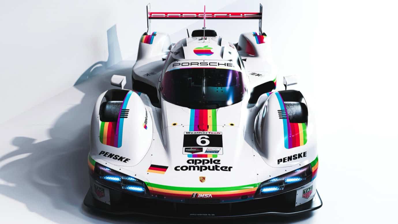 A white Porsche race car with a rainbow stripe and 'Apple Computer' logo. Number 6 on the hood, 'Penske' on sides. German flag below logo. Sleek, aerodynamic design.